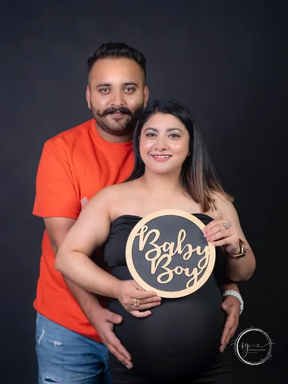 A joyful announcement for a baby boy. Using props like this "Baby Boy" sign adds a fun and personal touch to your pregnancy announcement photos, captured against a classic dark backdrop.