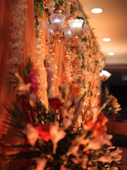 A detail shot from an indoor engagement setup, focusing on a vintage-style lamp fixture attached to the dense floral wall. This shows how we integrate lighting elements directly into our decor for a seamless, warm glow.