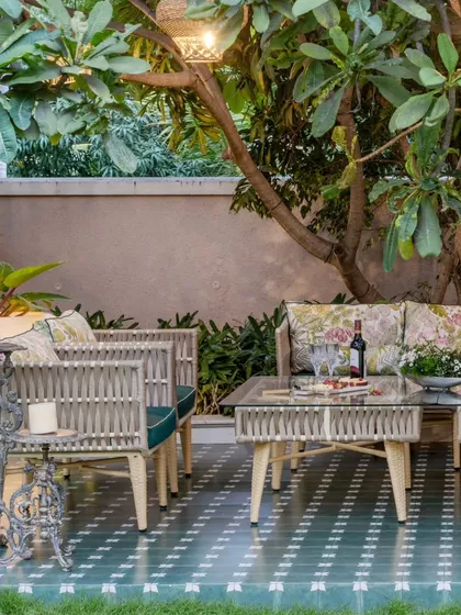An inviting outdoor lounge setup under a lush plumeria tree, designed for serene moments. The custom-made woven furniture, patterned tile deck, and carefully styled table create a perfect setting for relaxation, showcasing how I capture the essence of luxurious alfresco living.