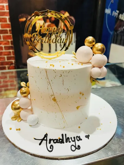 A chic and modern birthday cake with a white and rose gold color scheme and abstract gold details.