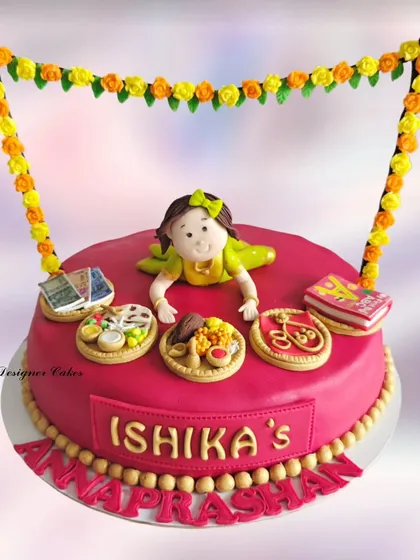 A traditional Annaprashan ceremony cake for a baby girl. This fondant cake features items used in the ritual, like books, money, and food, to symbolize the baby's future choices.