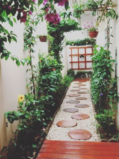 A perfect solution for a narrow walkway. This beautiful corridor garden features a path of round stepping stones set in white gravel, flanked by lush climbing plants and hanging baskets, creating a secret garden feel.