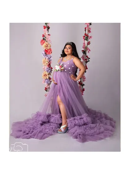 The full view of this gorgeous mama-to-be on the floral swing, showcasing the incredible length and texture of the purple ruffled gown.
