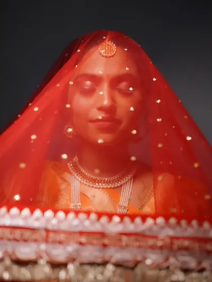 An artistic shot of the bride under her veil, highlighting the maang tikka and the soft, shimmering eye makeup.