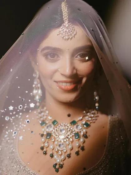 A moment of quiet joy behind the veil. The sparkle of the polki diamonds and the deep green of the emeralds in her bridal necklace create a captivating contrast, a true heirloom piece for a cherished memory.