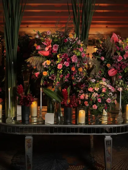 A floral fantasy for a sangeet night. This tablescape features an abundance of rich, colorful blooms in elegant vases, surrounded by the soft, warm glow of candles on a mirrored table.
