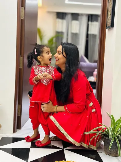 A candid moment of joy between a mother and her mini-me. They are both wearing our custom-designed tomato red peplum kurta and tulip pants sets, a vibrant and playful choice for any celebration. The daughter's outfit features delicate embroidery on the yoke.