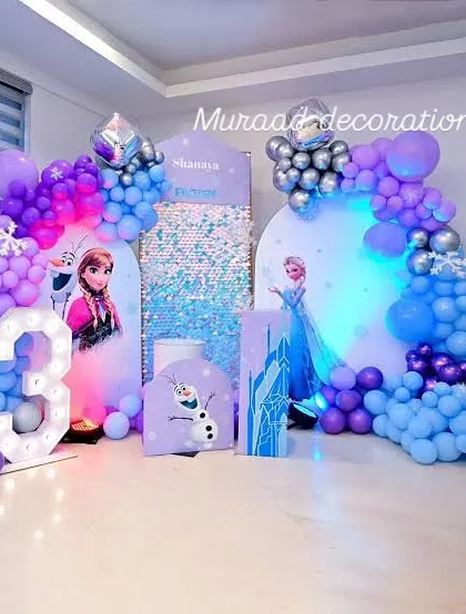This indoor Frozen party setup is all about the cool tones. We used multiple backdrops, a sequin panel, and character props, all tied together with blue, purple, and silver balloon arches and a large marquee number.