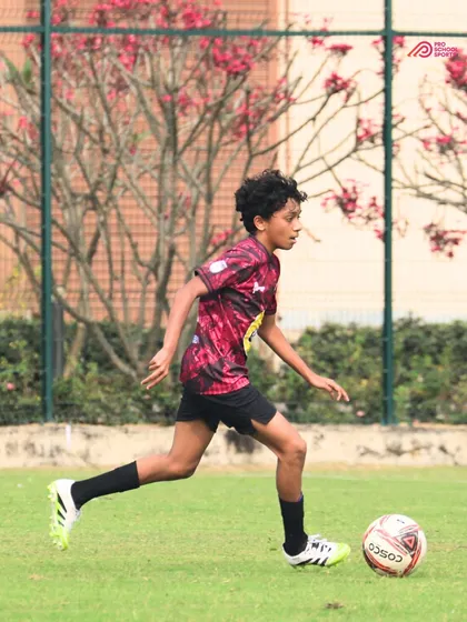 A young player runs with the ball against a beautiful backdrop, fully absorbed in the game.