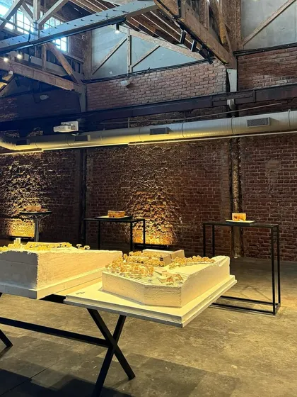 The exhibition space at IF.BE, featuring physical models of our projects. The raw brick walls and concrete floor of the restored ice factory provide a powerful backdrop for the refined architectural models.