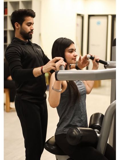 A trainer assists a member with her form on the shoulder press machine, helping her build strength safely.