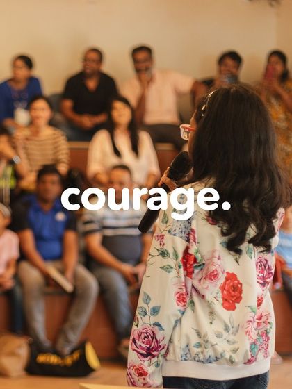 Courage. A young girl confidently speaks into a microphone in front of an audience of parents and peers. Our programs are designed to help children find their voice.