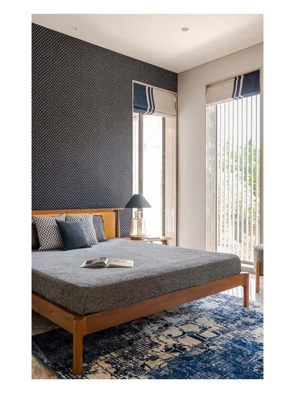 A bedroom in the "Solid | Void | Solid House" uses a combination of textures and patterns to create a cozy and sophisticated atmosphere. Large windows connect the room to the garden outside.