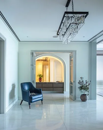 This elegant hallway in 'The 18th' project in Gurgaon uses classic paneling and a striking chandelier to create a grand entrance. The design balances traditional elements with modern touches, like the bold green armchair that adds a pop of color.