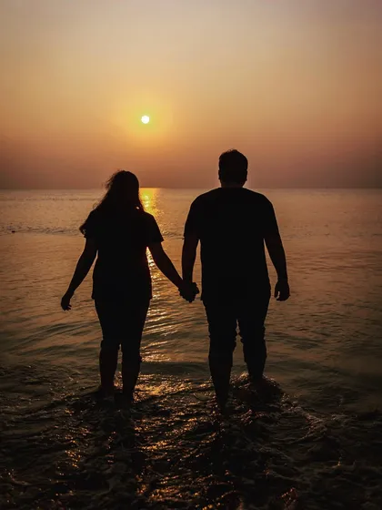 A classic silhouette of the couple holding hands as they walk into the sea towards the setting sun. A timeless and romantic pre-wedding photograph.