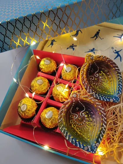 A custom Diwali hamper box with hand-painted diyas, Ferrero Rocher chocolates, and festive fairy lights.