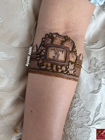 The completed armband for a 'Mom to Be' mehendi. This design is filled with adorable baby-themed motifs like teddy bears, onesies, and feeding bottles, all framed within a decorative border.