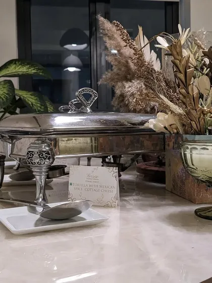 An elegant silver chafing dish keeping our hot appetizers at the perfect temperature, set next to a rustic floral arrangement for a touch of natural beauty.