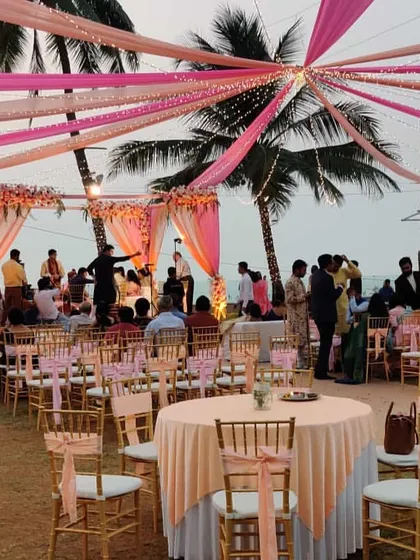 This wide shot shows the full scale of an outdoor beach engagement. You can see the pink-themed canopy draping, the main ceremony mandap, and the organized guest seating arrangement, all set up on the lawn adjacent to the beach.