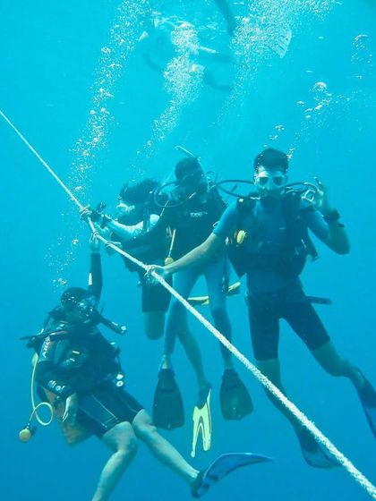 Students hold onto a guide rope during their first open water dive. This is a standard safety procedure that helps divers stay together and control their descent.