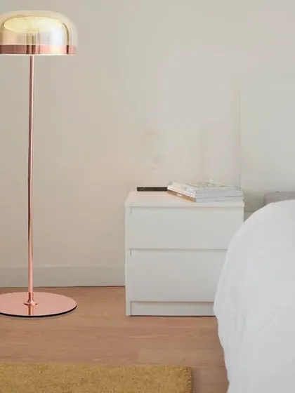 This dainty metal floor lamp features a sleek copper finish and a glass dome shade. Its minimalist design is perfect for a modern bedroom or living space, providing soft, ambient light without taking up much space.
