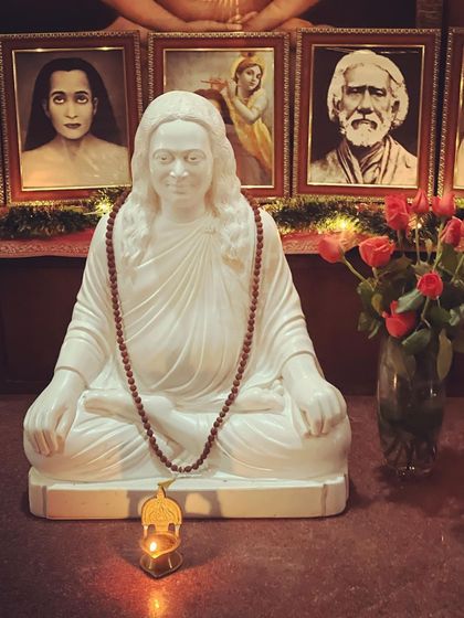 A close-up of the Mahavatar Babaji statue on our altar, with a single candle flame and fresh roses. This simple arrangement inspires a feeling of deep peace and reverence for the deathless guru.