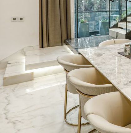 A view from the dining area looking towards the staircase, showing the clean lines of the marble floor and the elegant, modern dining chairs.
