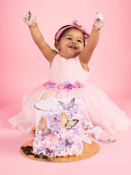 Pure joy and celebration as a little girl, dressed in a lovely pink frock, throws her hands up in delight during her butterfly-themed first birthday cakesmash. These sessions are all about capturing personality and fun.