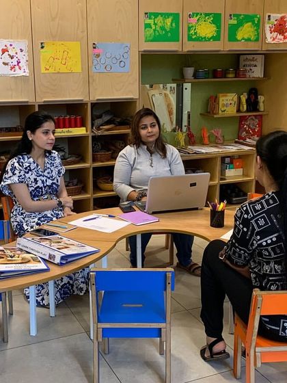 Two parents sit with an educator to discuss their child's progress, with learning portfolios on the table. We use these conferences to share detailed insights and collaborate on strategies to support the child both at school and at home.