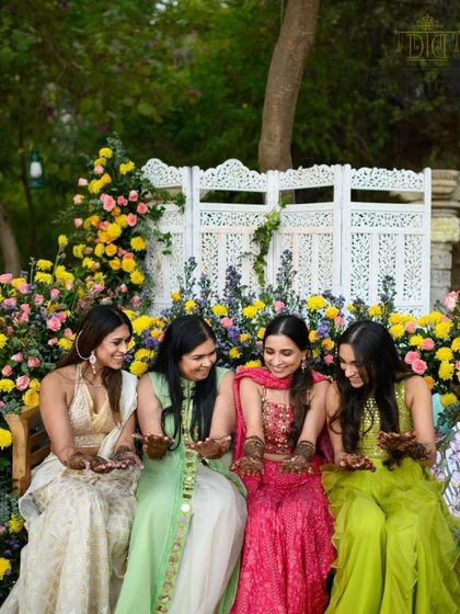 A bride shares a laugh with her bridesmaids during her Mehendi. We design beautiful backdrops, like this one with yellow and pink flowers, to create perfect photo opportunities for these cherished moments.