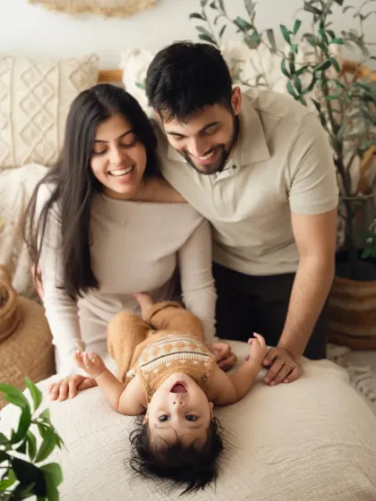 Parents look on with delight as their baby lies upside down, giggling. This playful shot is a great example of a fun, lifestyle family photoshoot.