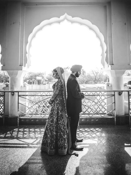 A black and white silhouette of a Sikh couple standing back-to-back in an archway, creating a powerful and symmetrical image.
