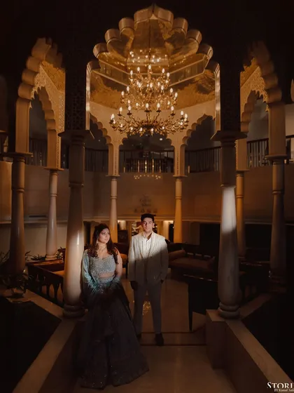 A dramatic portrait of Rupen and Shikha in a grand, chandelier-lit hall, the lighting creating a sense of awe.