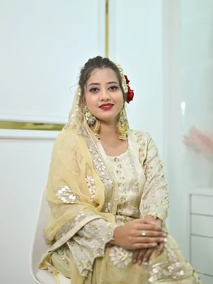 A smiling model seated in a white chair, wearing the ivory sharara set. The simple setting allows the detailed outfit to shine.