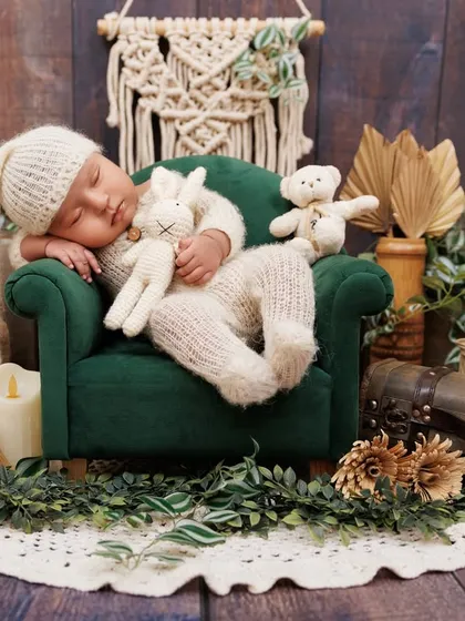 A newborn in a cozy bunny outfit sleeps on a miniature green sofa, surrounded by rustic and natural props.