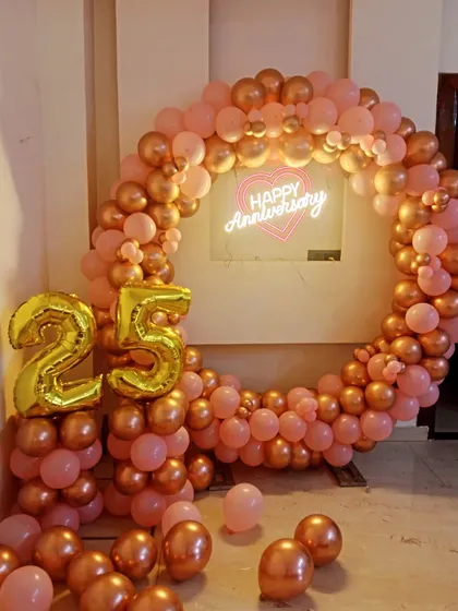 Rose gold is a popular and elegant choice for anniversary decorations. Here is a full circular balloon arch with a "Happy Anniversary" neon sign and a "25" marquee number, creating a beautiful focal point for the event.