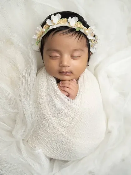 Simplicity at its best. A baby swaddled in white on a bed of soft, white tulle fabric. The floral headband adds a delicate touch to this angelic portrait.
