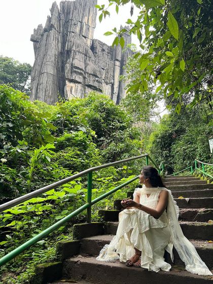 A trekker sitting on the steps of the unique Yaana caves, surrounded by lush greenery.