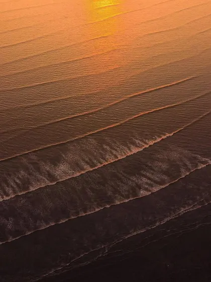 A close-up aerial shot of golden waves at sunset, highlighting the beautiful lines and textures of the water.