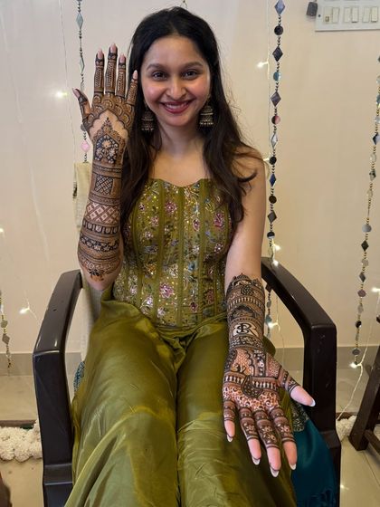 A happy bride showing off her freshly applied mehendi. The intricate design covers her full arms, ready to transform into a beautiful dark stain.