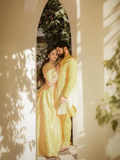 An intimate portrait of a couple in matching yellow outfits, framed by a sunlit archway. This photo captures a quiet, romantic moment during their Haldi ceremony celebrations.