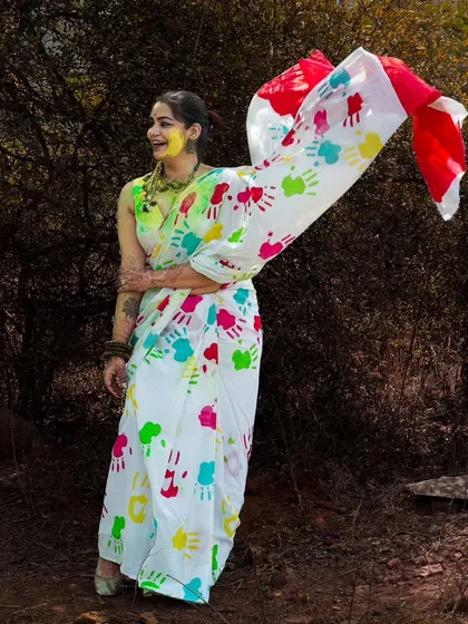 A joyful, candid moment from the Holi photoshoot. The model's genuine smile and the flowing saree create a feeling of celebration and happiness.