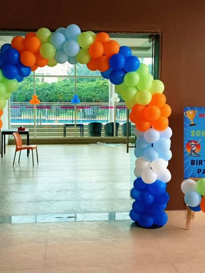 A colorful balloon arch for a cricket-themed birthday party, using the team colors of blue, green, and orange.