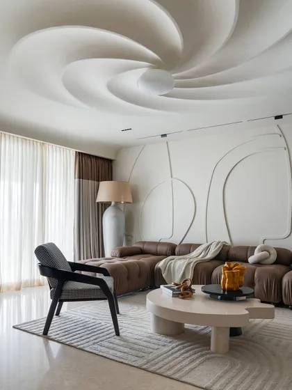 In this residential living room, the ceiling becomes a sculptural centerpiece. The swirling form creates a sense of movement and draws the eye upward, transforming a flat surface into a dynamic work of art. This feature, combined with the abstract wall molding, establishes a bold and eccentric personality for the home.