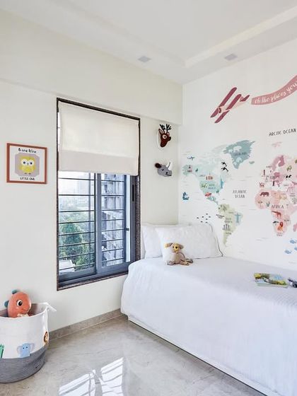 This enchanting children's room features a large world map wall decal to spark young imaginations. The serene white space is adorned with charming framed artworks and a soft cloud-shaped light.