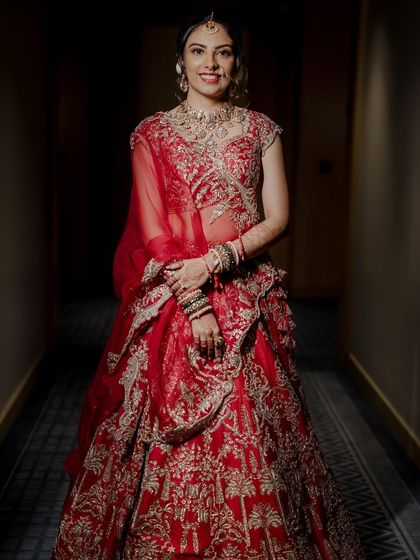 A full-length shot of the bride in her stunning red Anushree Reddy lehenga. The makeup is designed to be flawless and long-lasting, ensuring she looks perfect from every angle.