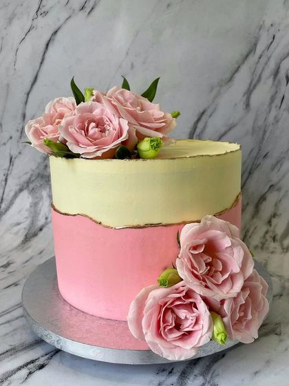 A simple and beautiful design featuring two-toned pastel pink and yellow buttercream with a delicate fault line edged in gold. The fresh pink roses add a touch of natural beauty.
