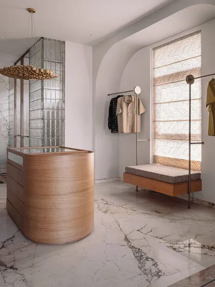 This walk-in wardrobe and bathroom was designed to feel like a high-end SoHo boutique. It features a sculptural, monolithic marble basin, an island dresser, and custom clothing racks, all set against a backdrop of luxurious veined marble.