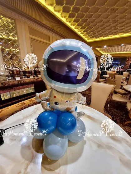 A space-themed table centerpiece featuring an astronaut foil balloon on a base of blue and silver balloons.