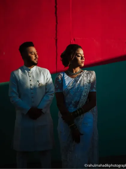 A dramatic portrait using harsh light and shadow. The couple stands against a bold red and teal wall, creating a high-fashion, editorial-style image that is both modern and striking.